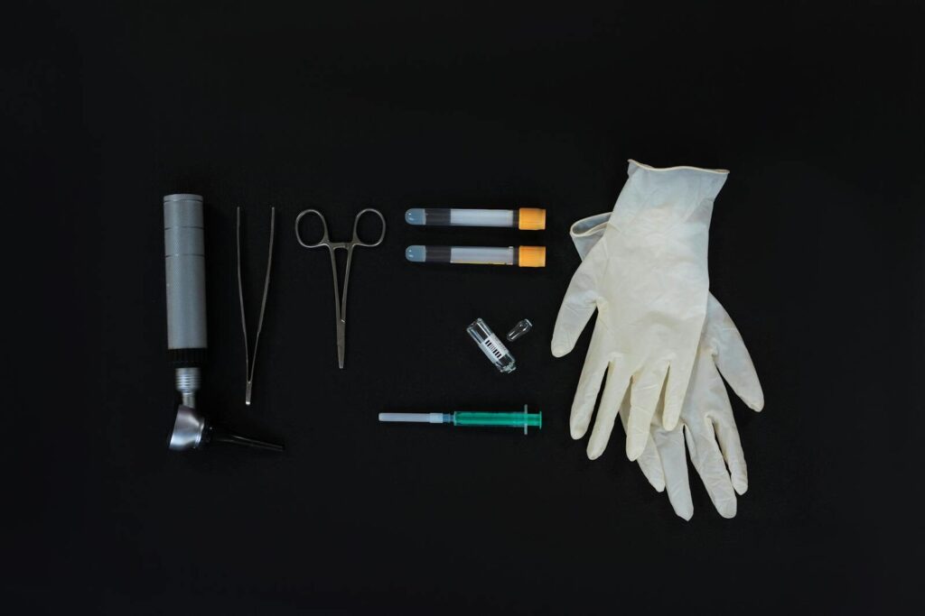 Flat lay of essential medical tools on a black background, including gloves and syringe.